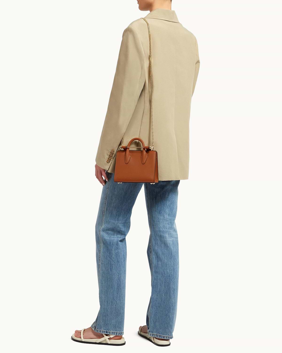 Short gold chain strap attached to small brown leather top-handle bag, worn cross-body.