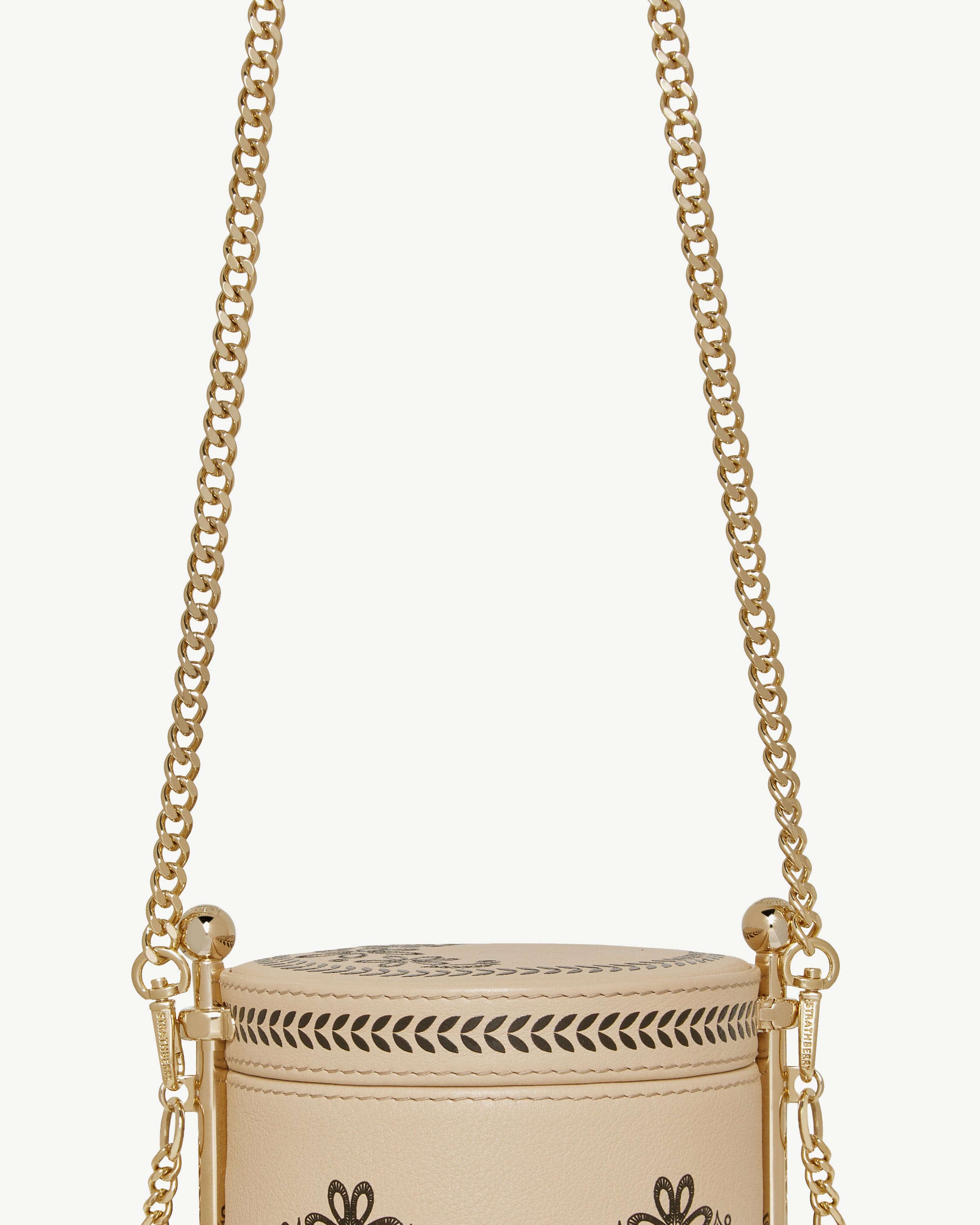 Gold short chain strap attached to beige cylindrical bag with decorative cutouts.
