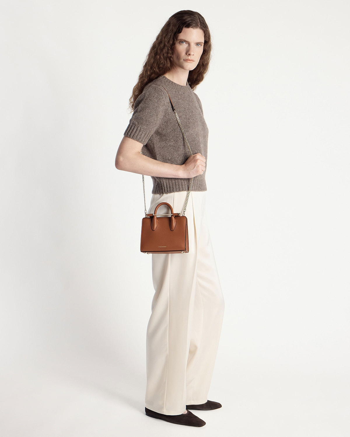 Model wearing brown knit top and cream trousers holding chestnut nano tote with chain strap.