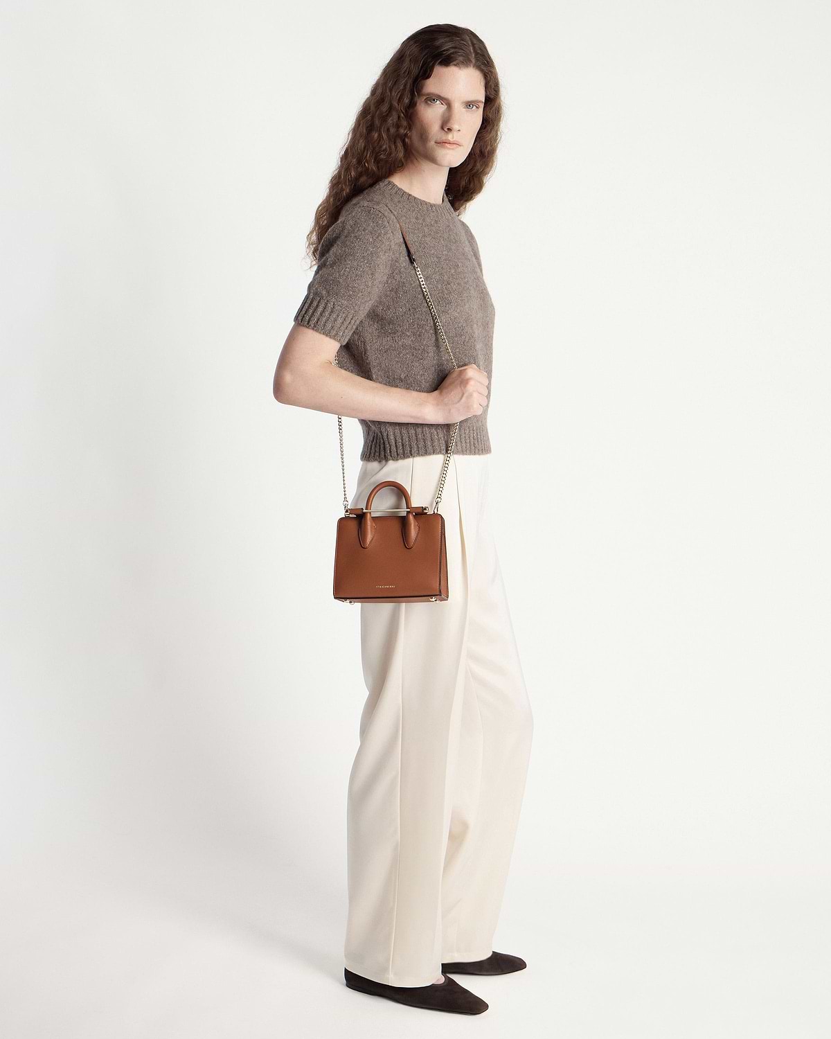 Model wearing brown knit top and cream trousers holding chestnut nano tote with chain strap.
