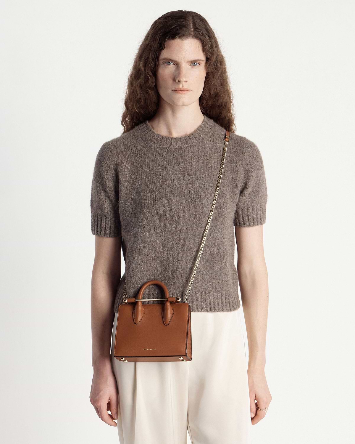Woman in brown jumper wearing chestnut Strathberry nano tote with gold chain