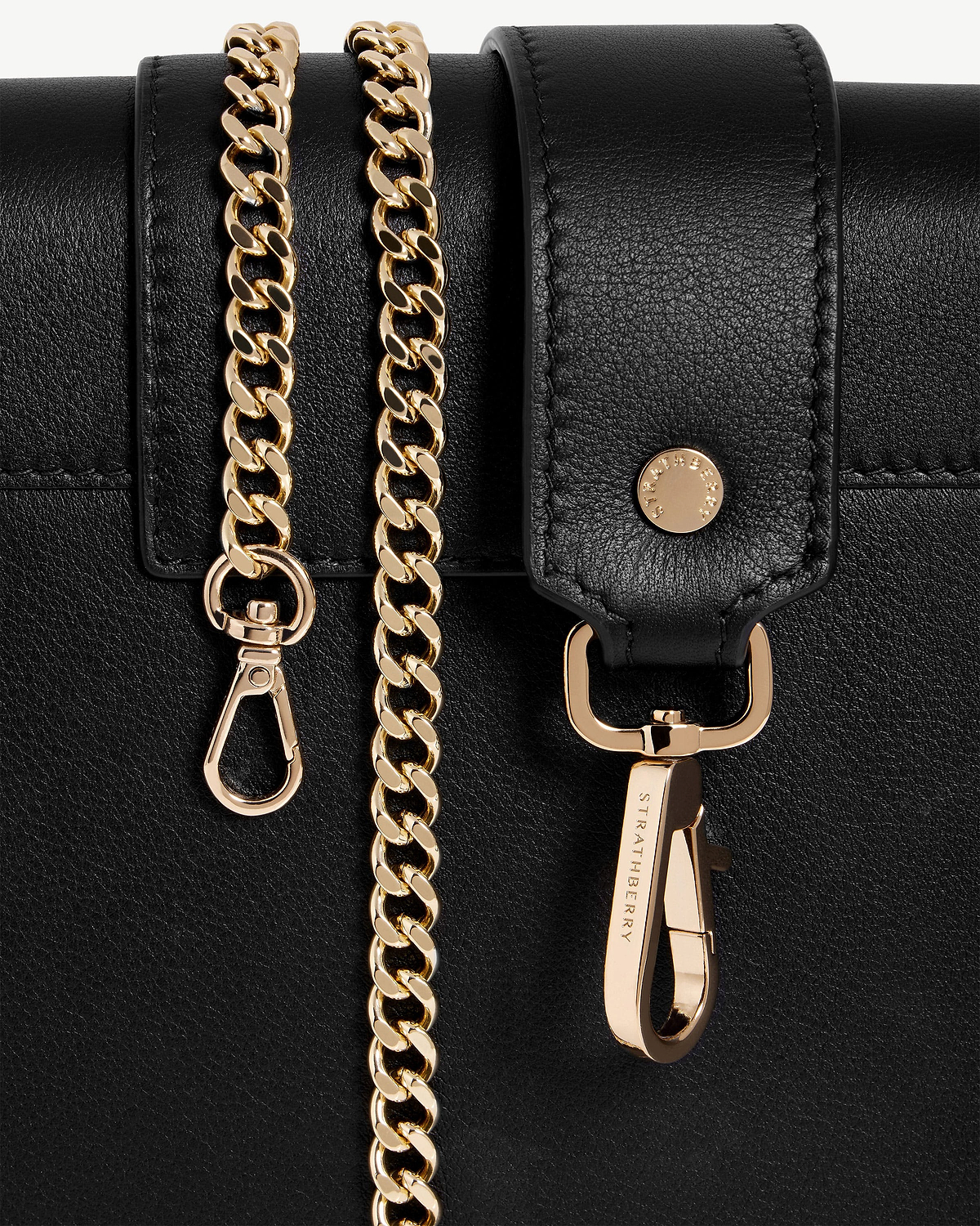 Black leather bag detail with gold chain and Strathberry engraved clasp.