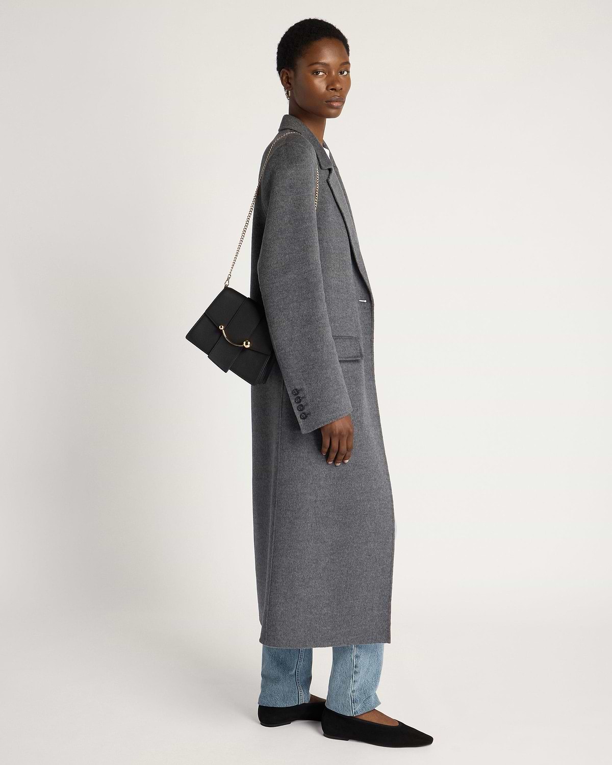 Model in grey long coat carrying black Box Crescent bag with gold chain