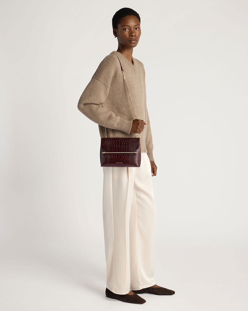 Model wearing croc-embossed burgundy crossbody bag with gold chain strap.