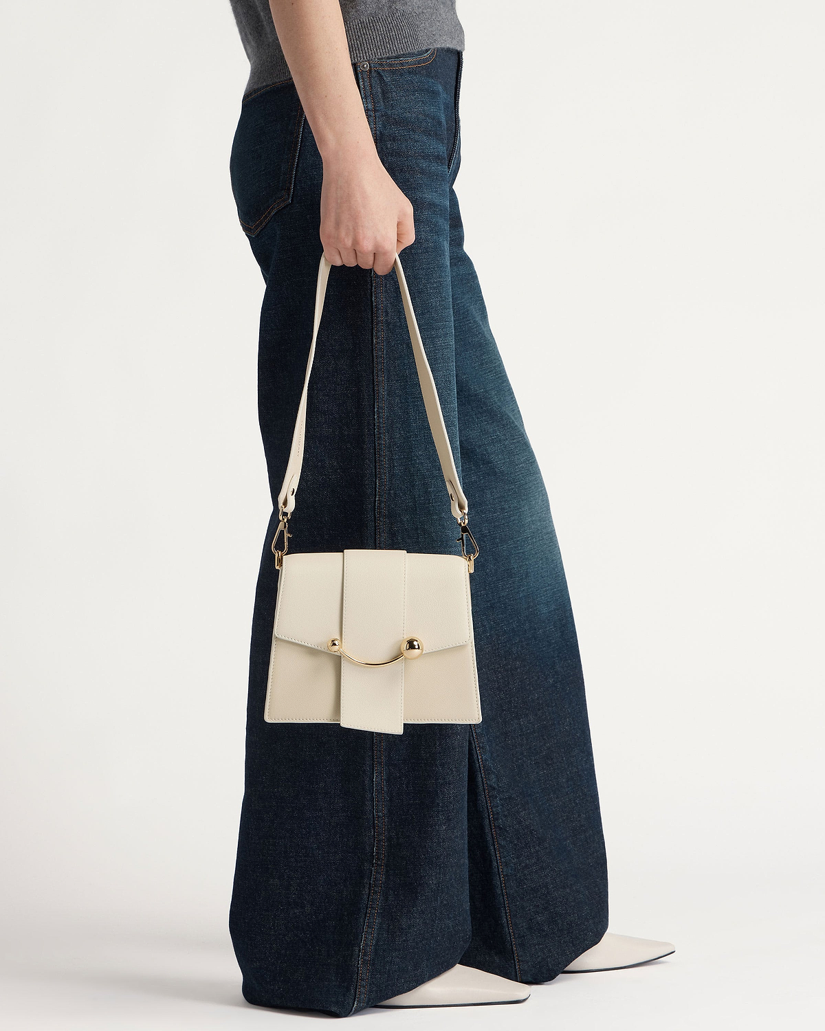 Model holding vanilla box handbag with gold crescent bar and strap.