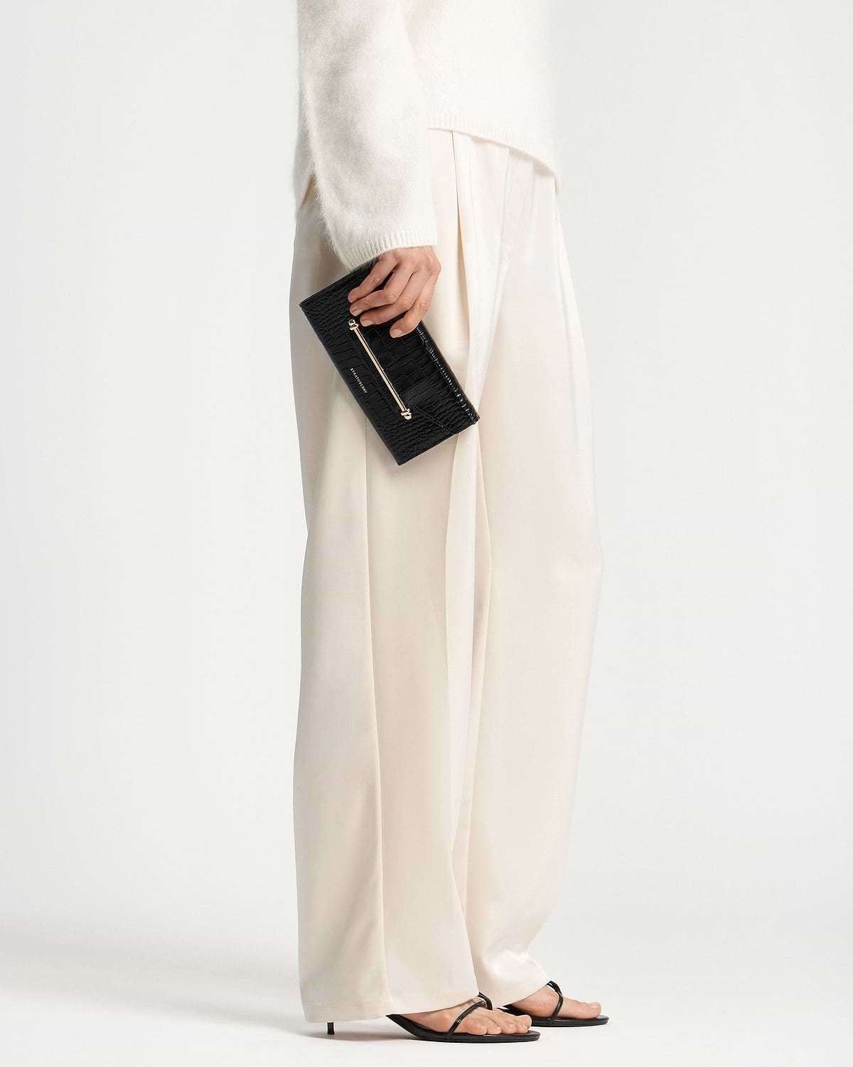 Hand holding black croc-effect textured wallet with gold bar detail