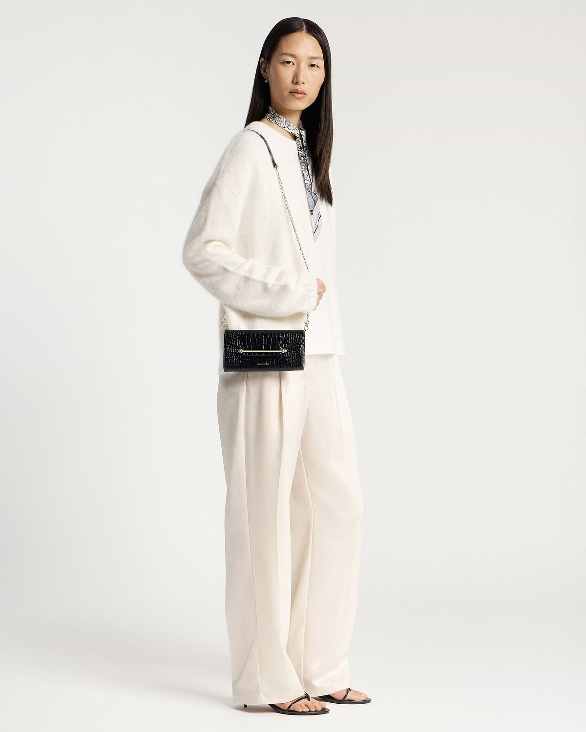 Model wearing a black crocodile-effect chain wallet with a gold chain strap.