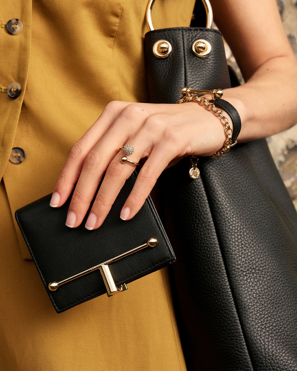 Model's hand holding a black leather wallet with gold bar detail.