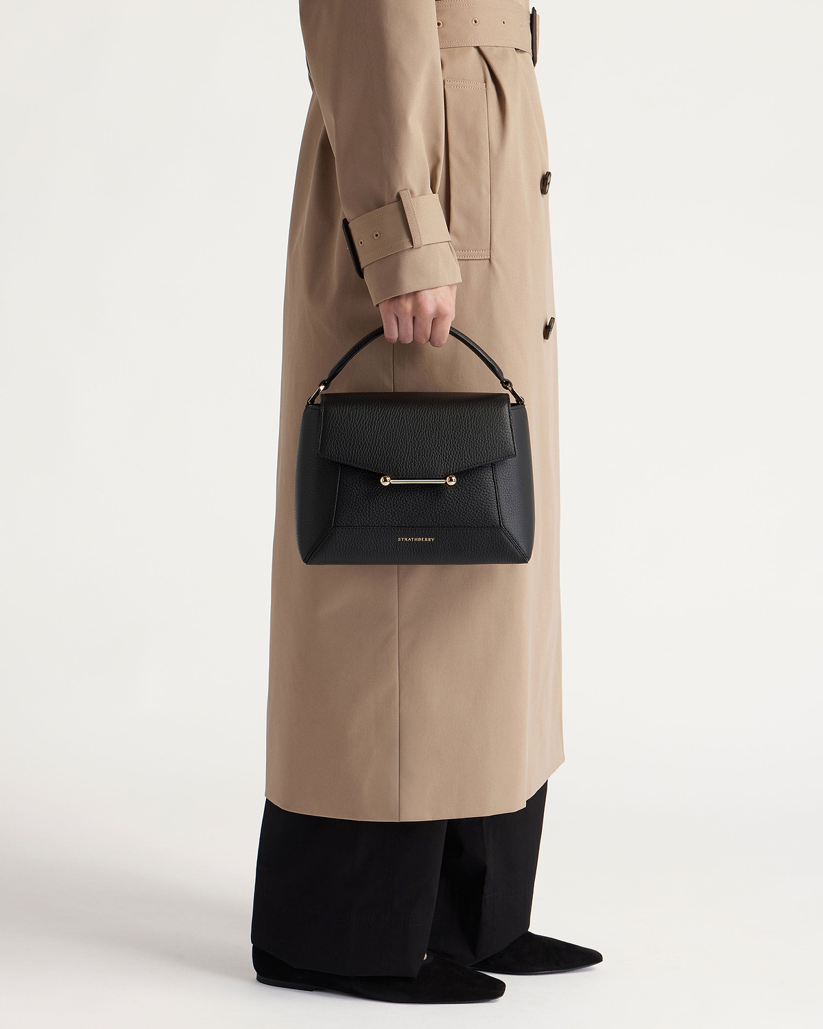 Black Strathberry mosaic bag with top handle and gold bar, held by model.