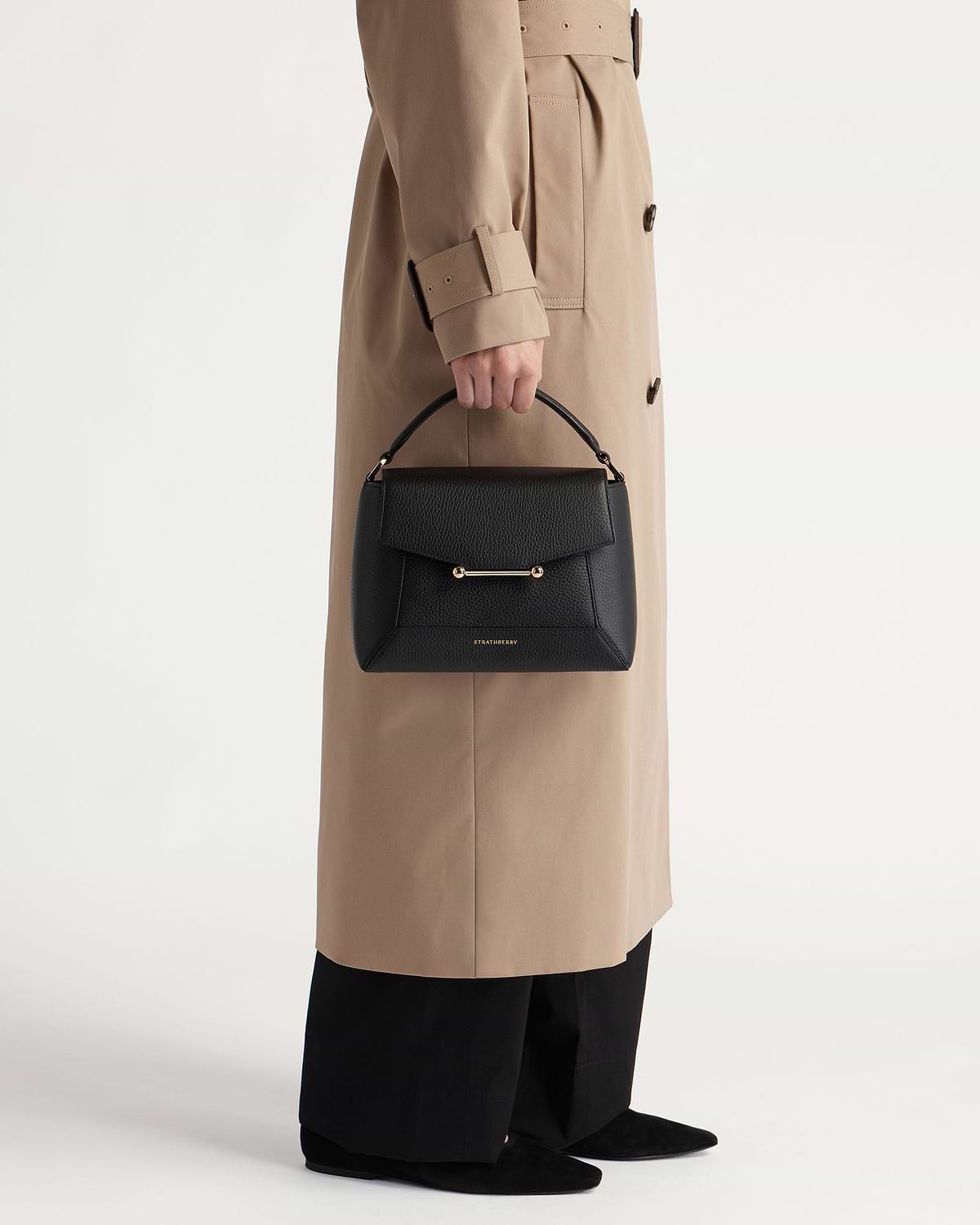 Black Strathberry mosaic bag with top handle and gold bar, held by model.