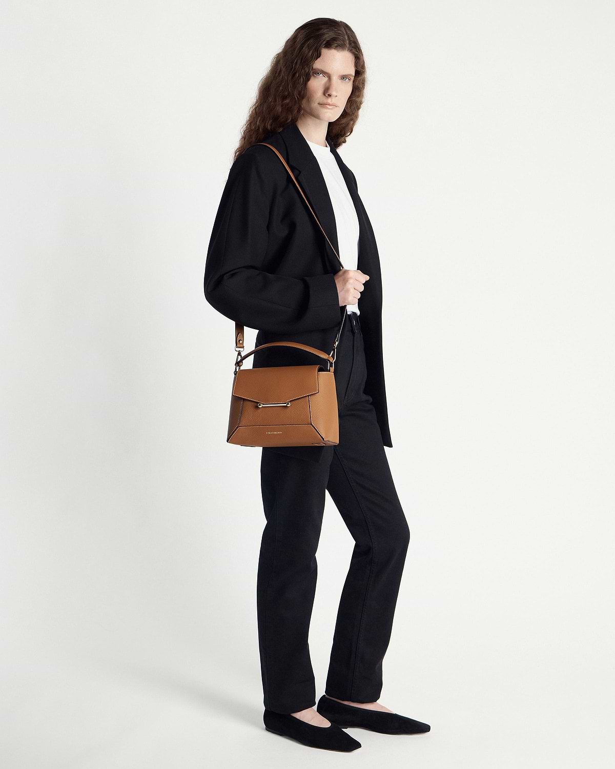 Model wearing black blazer carrying tan mosaic bag with vanilla stitching over shoulder.