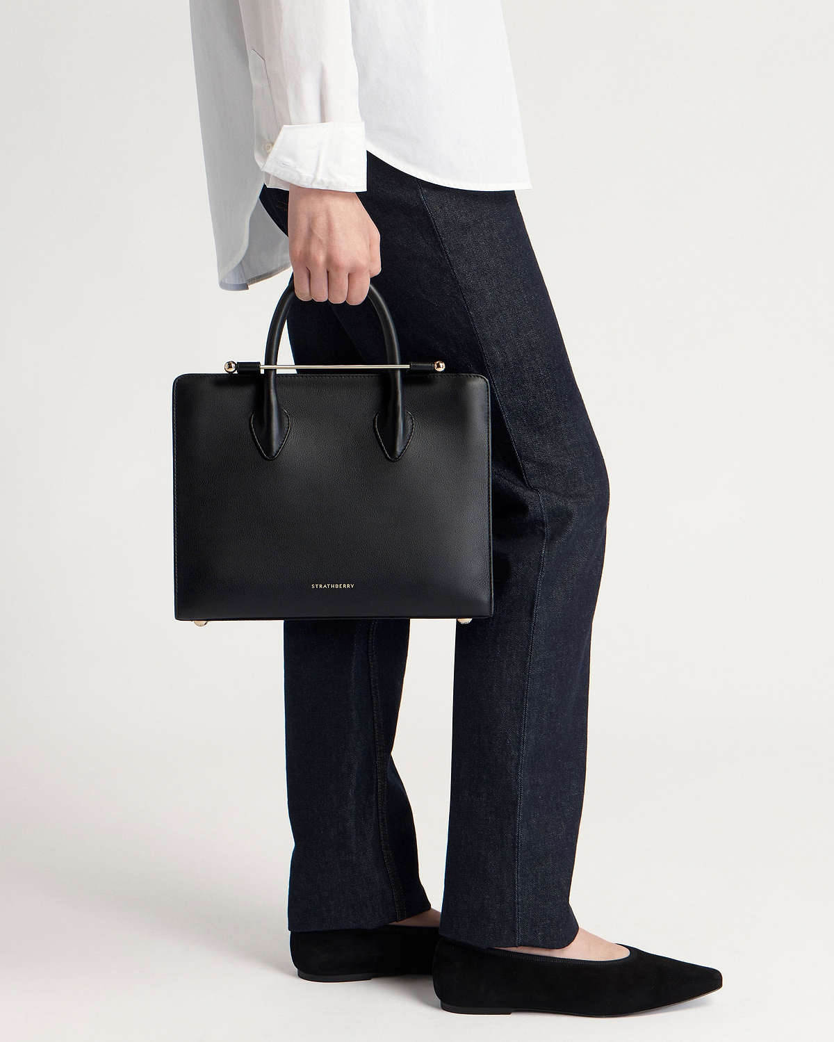 Black Strathberry midi tote with top handles and gold bar, held by model.