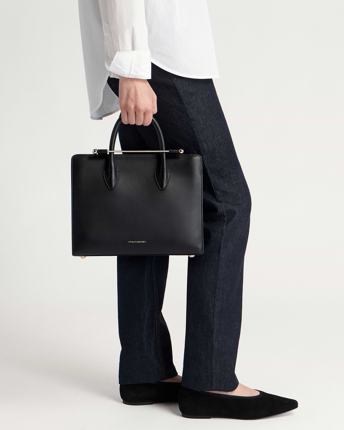 Black Strathberry midi tote with top handles and gold bar, held by model.