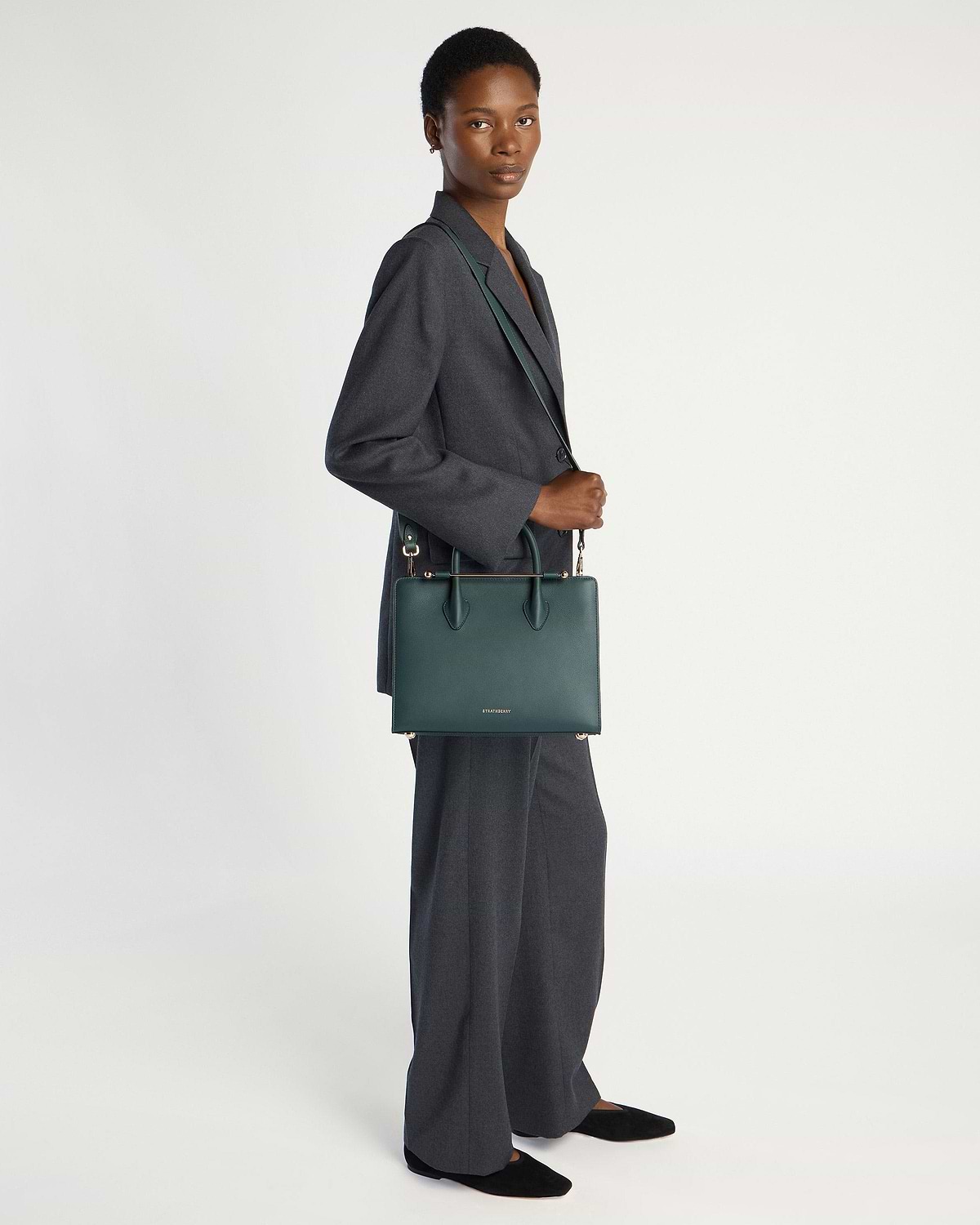 Model wearing a grey suit carrying a bottle green midi tote bag.