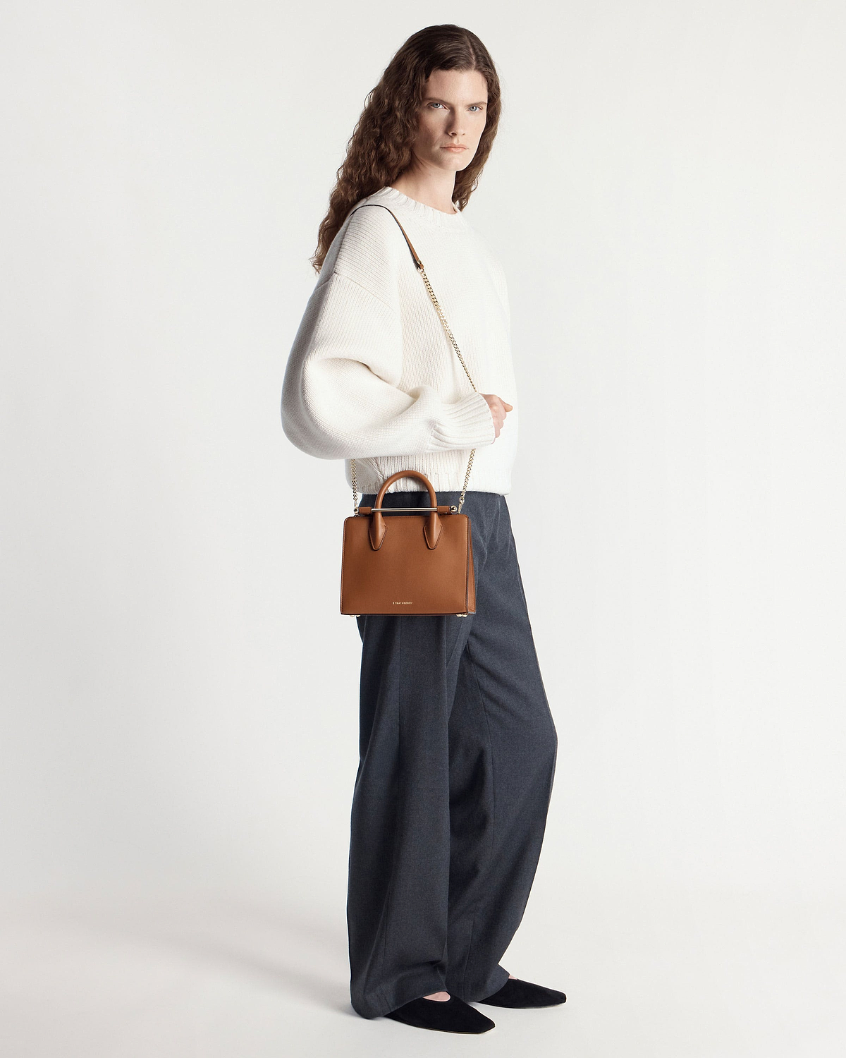Model wearing white jumper carrying a chestnut mini tote with chain strap.