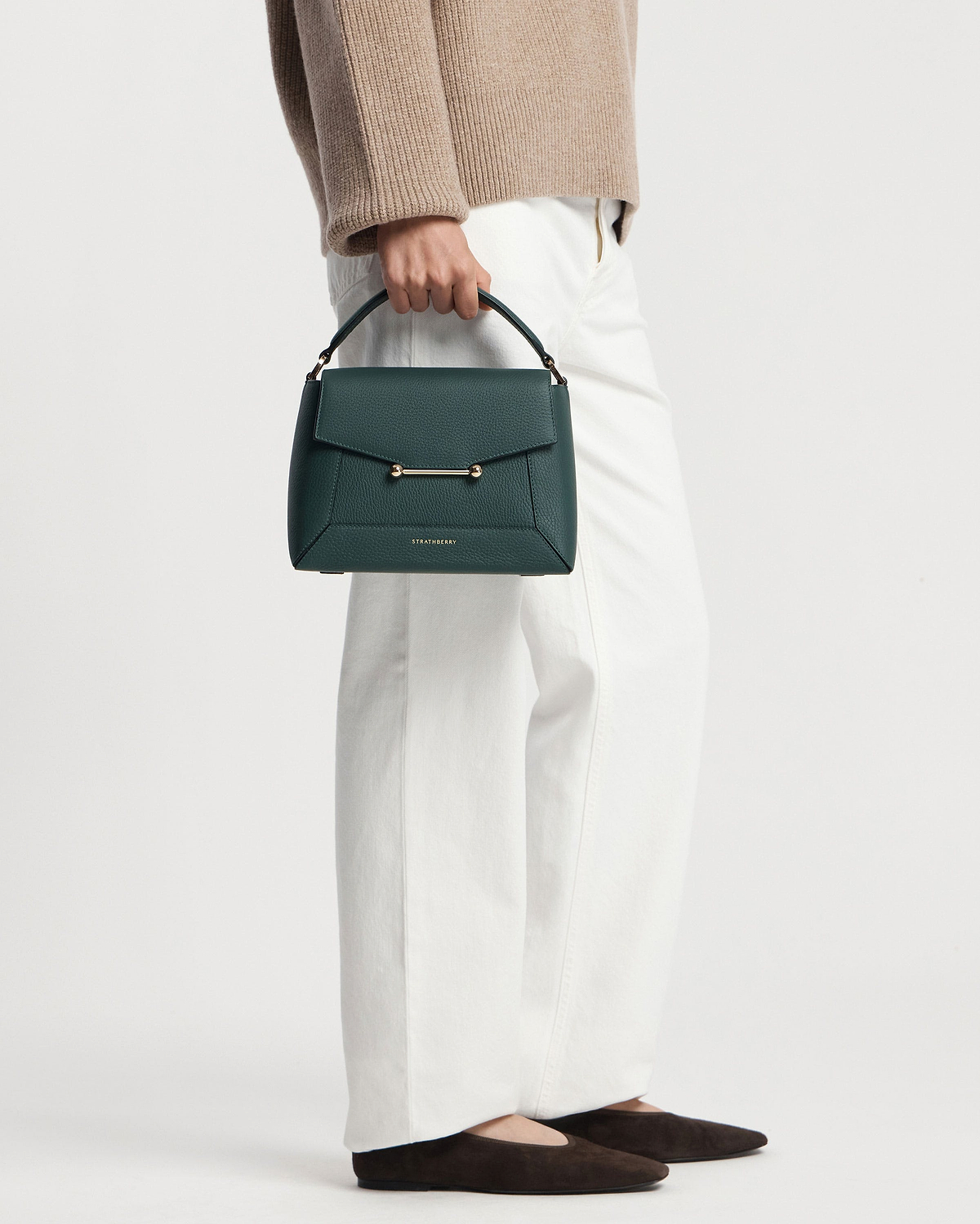 Model carrying bottle green Strathberry mosaic bag by the top handle.
