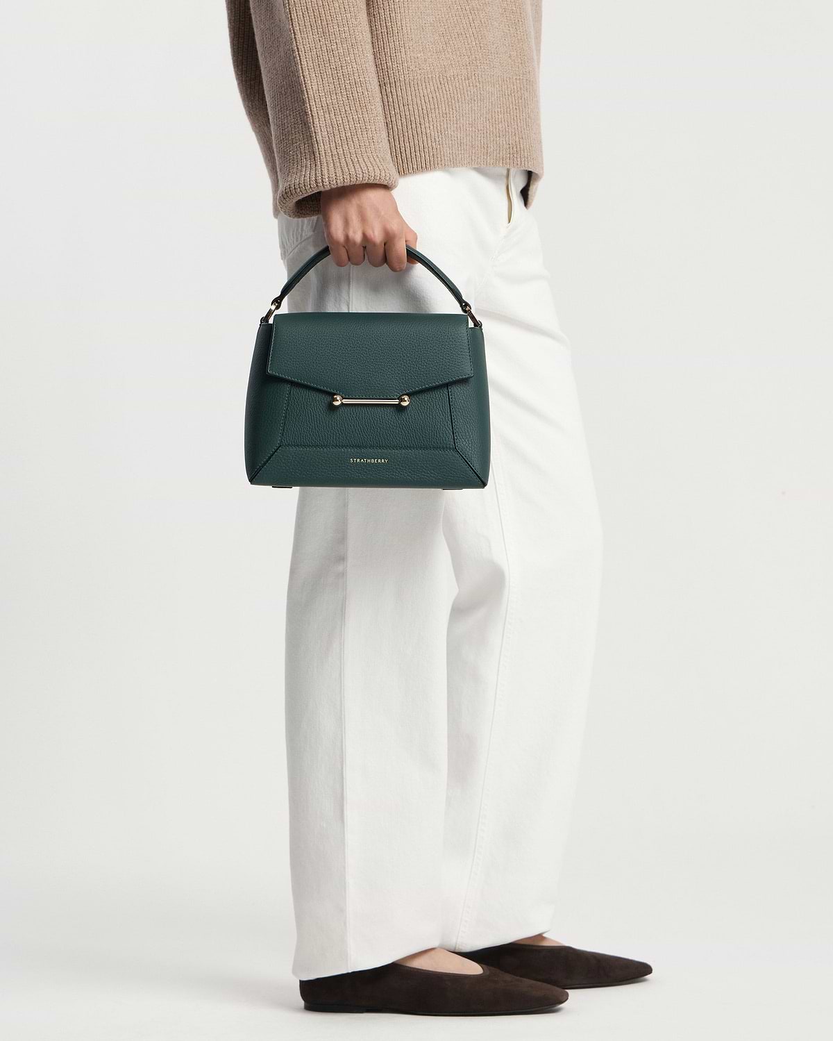 Model carrying bottle green Strathberry mosaic bag by the top handle.