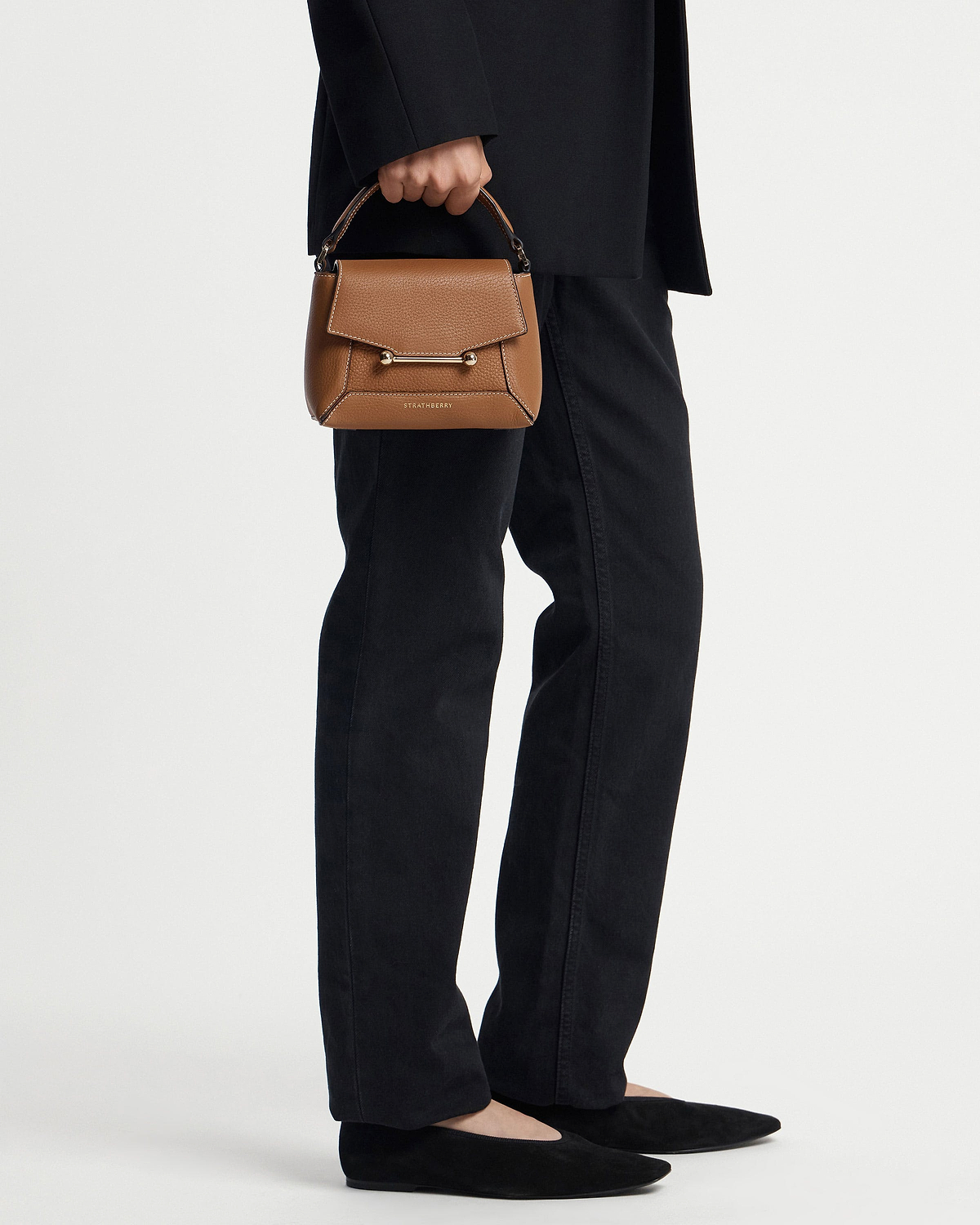 Tan Strathberry Mosaic Nano handbag with vanilla stitching held by model wearing black trousers.