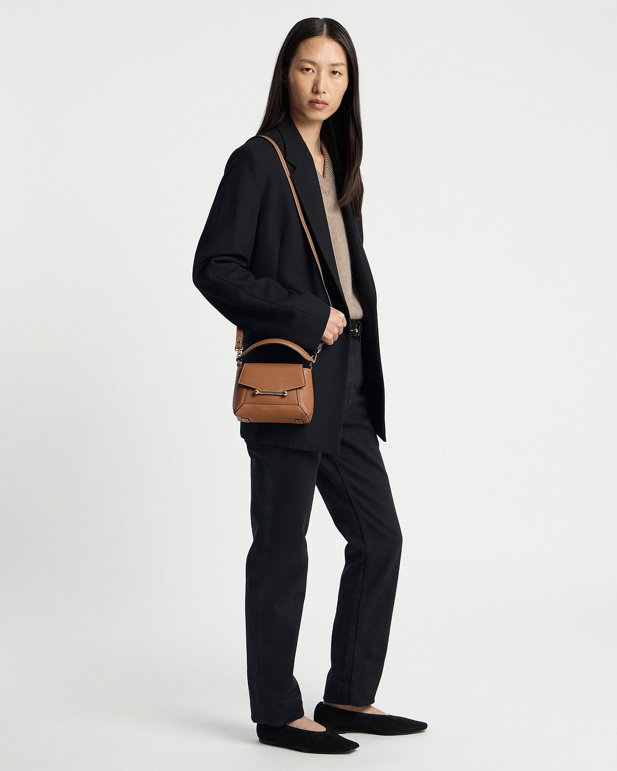 Woman wearing a black outfit carrying a tan top-handle crossbody bag with vanilla stitching.