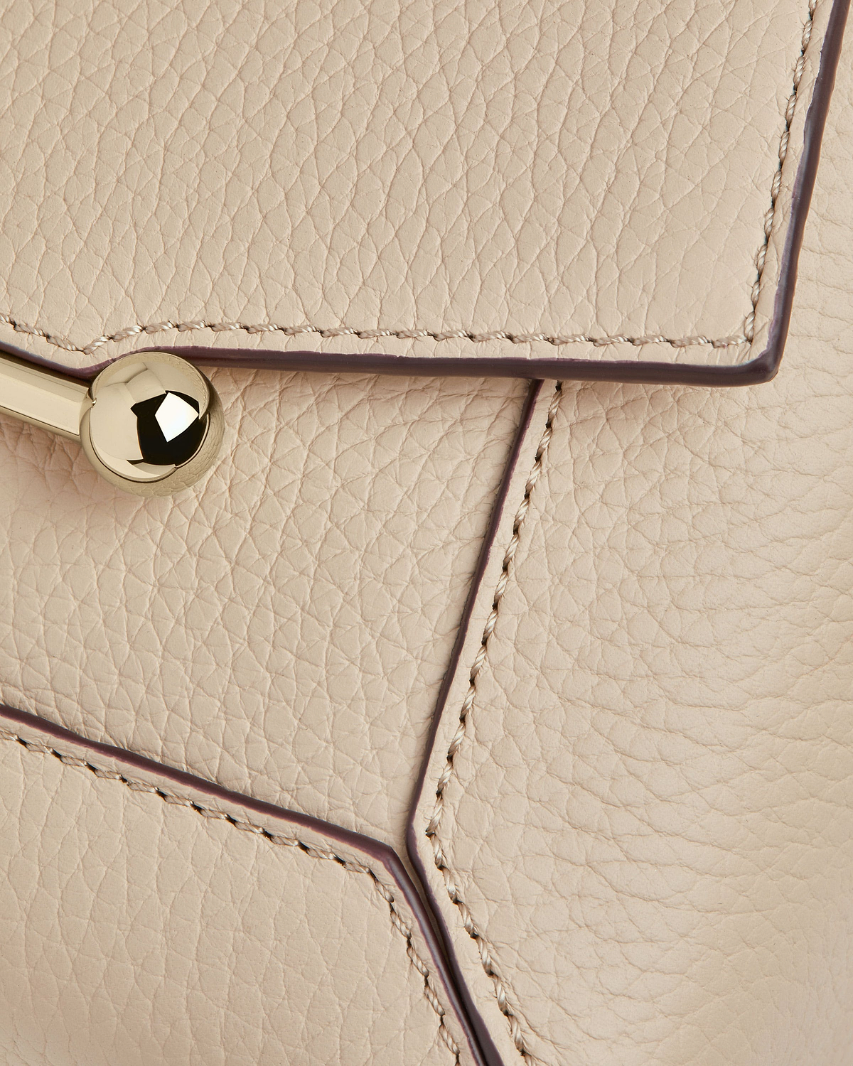 Oat-coloured leather bag showing pebbled texture, stitching and gold ball clasp.