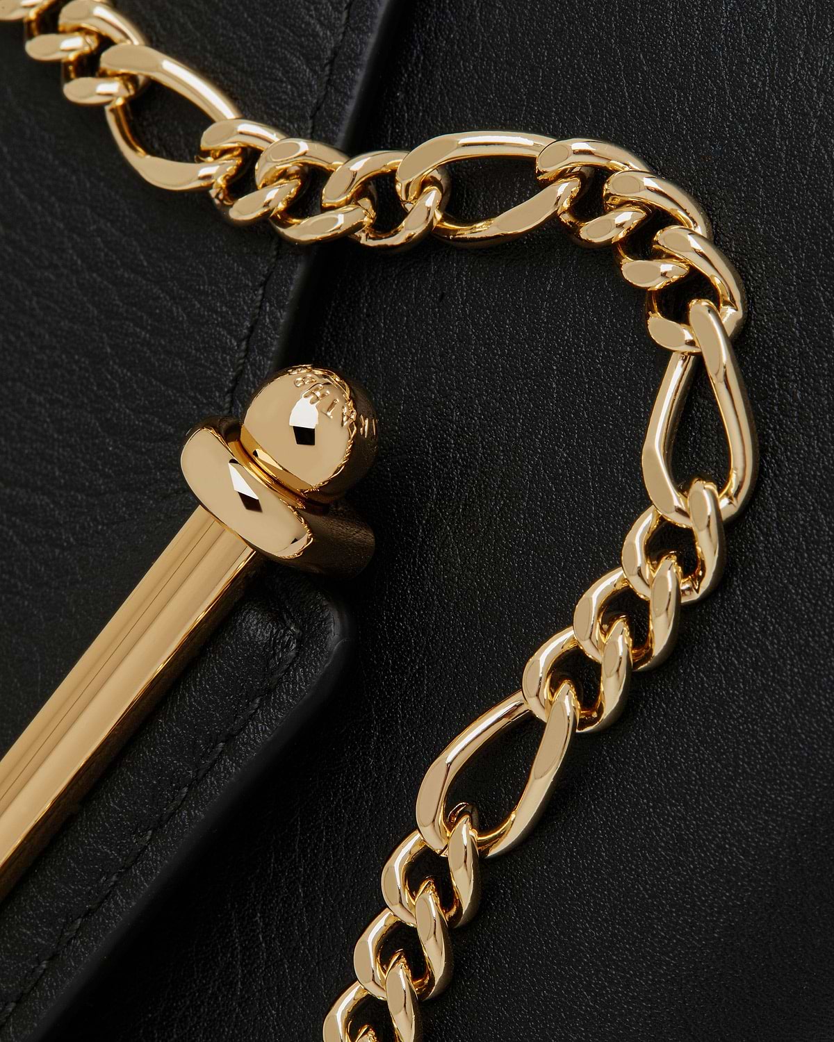 Gold chain and polished gold clasp on black grained leather wallet surface.