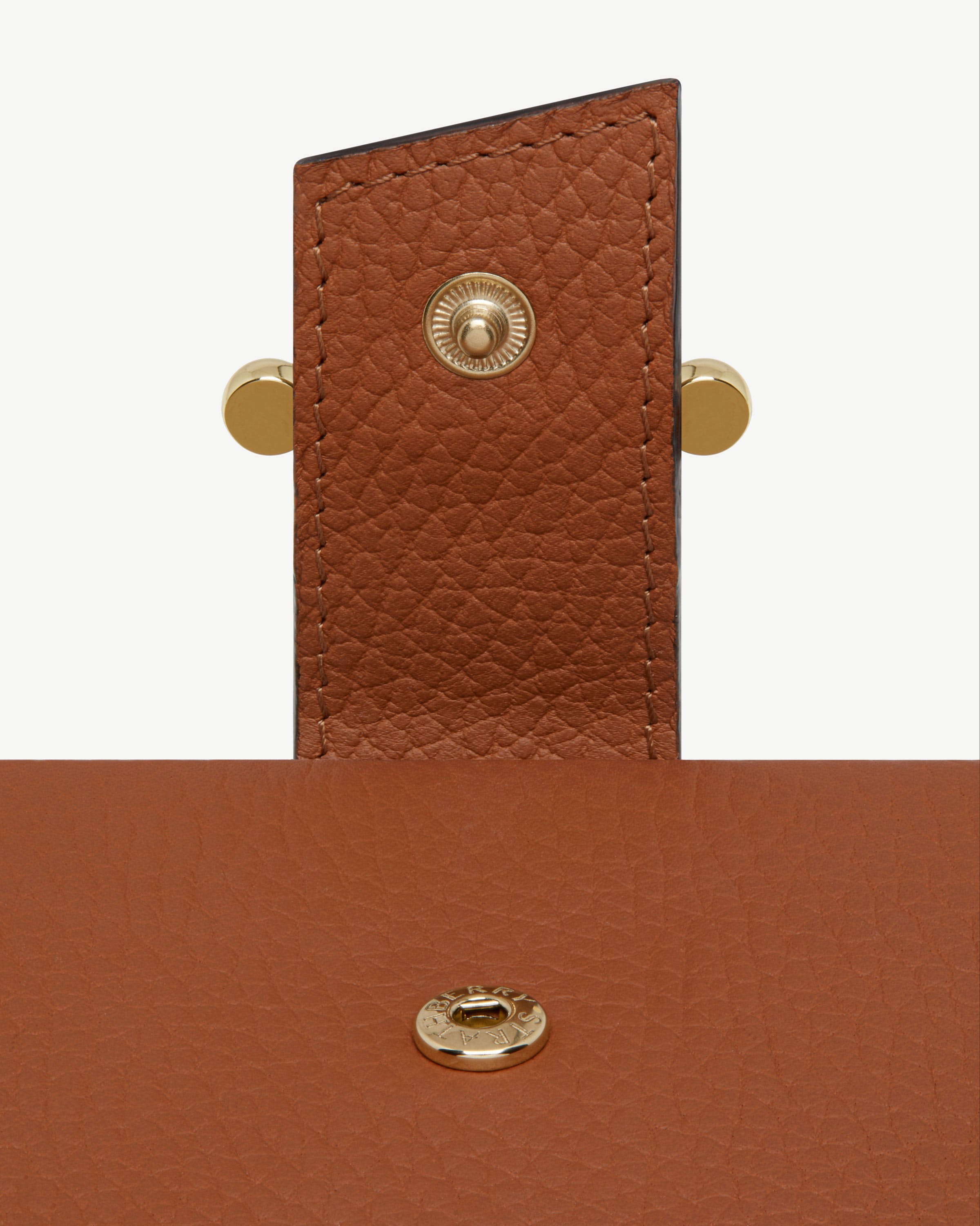 Tan leather notebook flap with gold snap and textured grain detail.