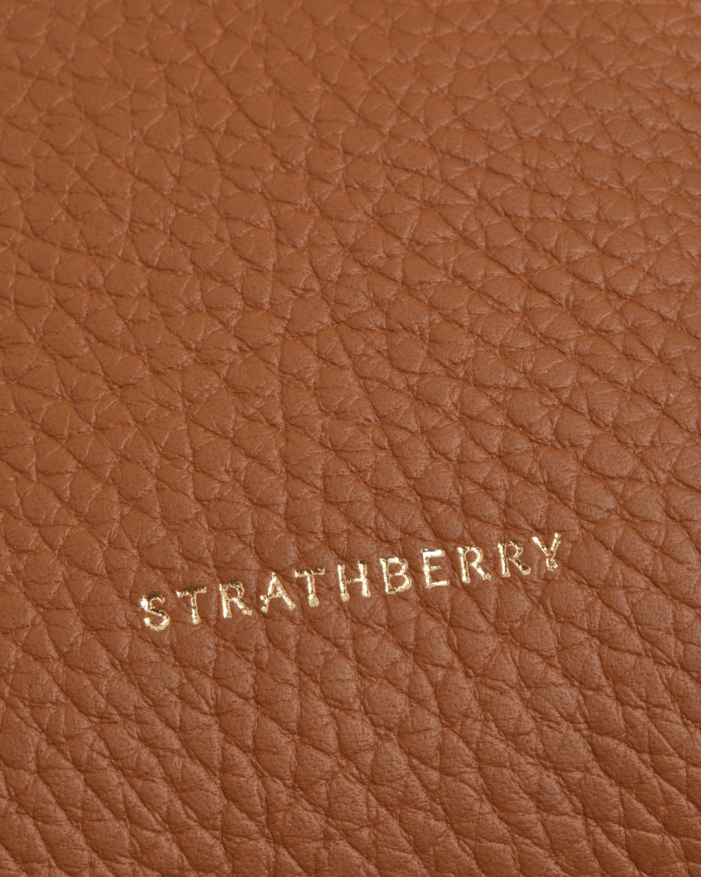 Close-up of tan pebbled leather with gold Strathberry logo lettering.