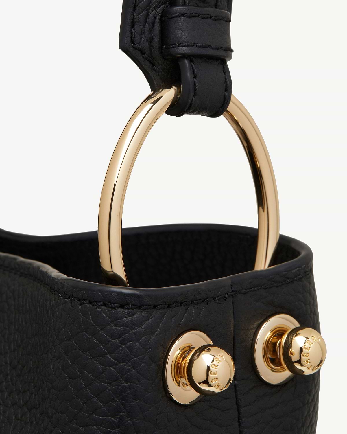 Black leather bag trim with gold ring and visible Burberry studs.