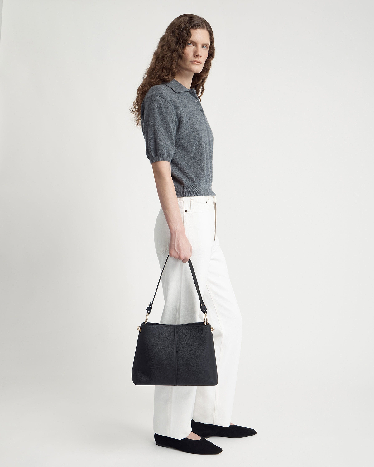 Model holding black hobo bag with single strap and gold hardware.