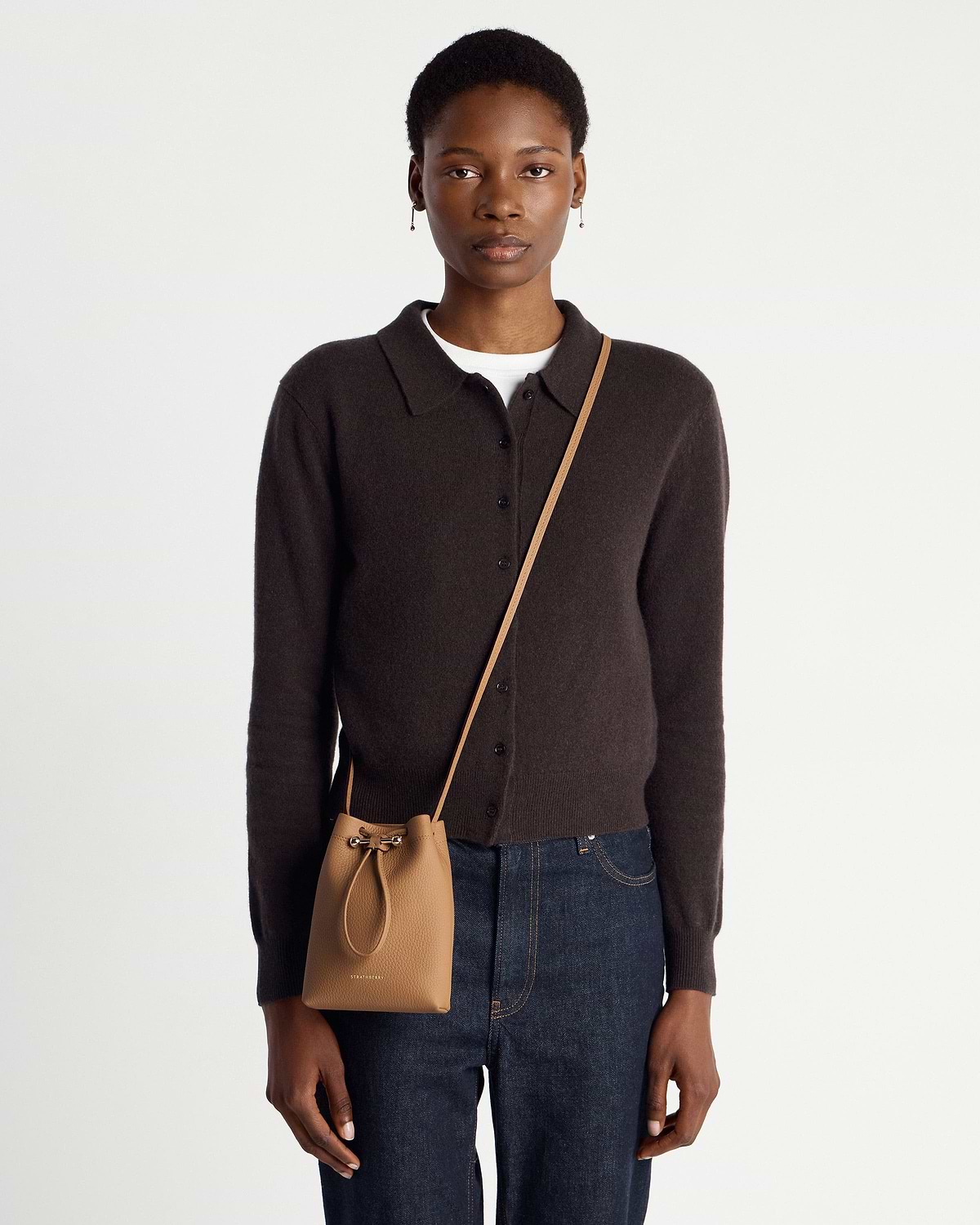 Model wearing a caramel leather drawstring crossbody pouch hanging at hip.