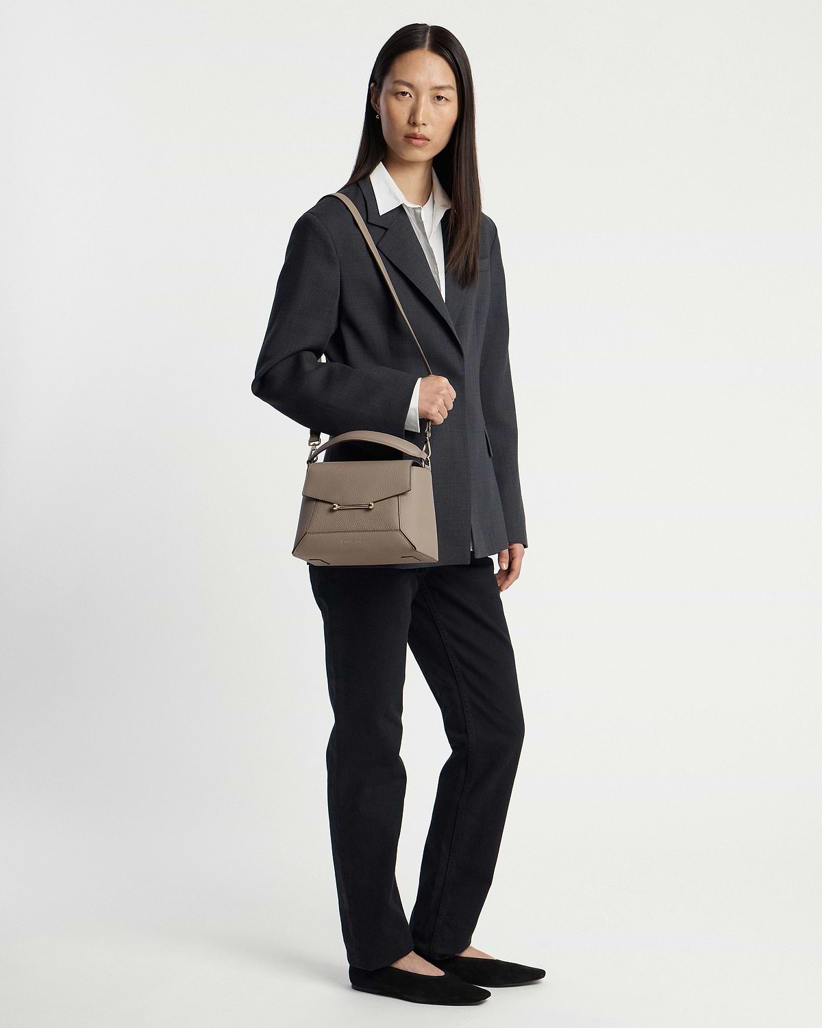 Model wearing dark blazer and black trousers holding taupe mosaic bag