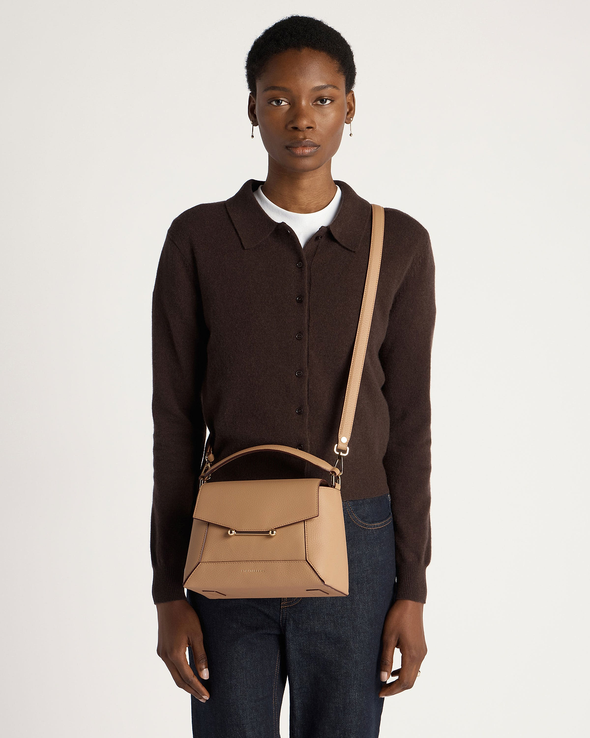 Woman wearing dark brown cardigan and jeans carrying a caramel mosaic crossbody bag.