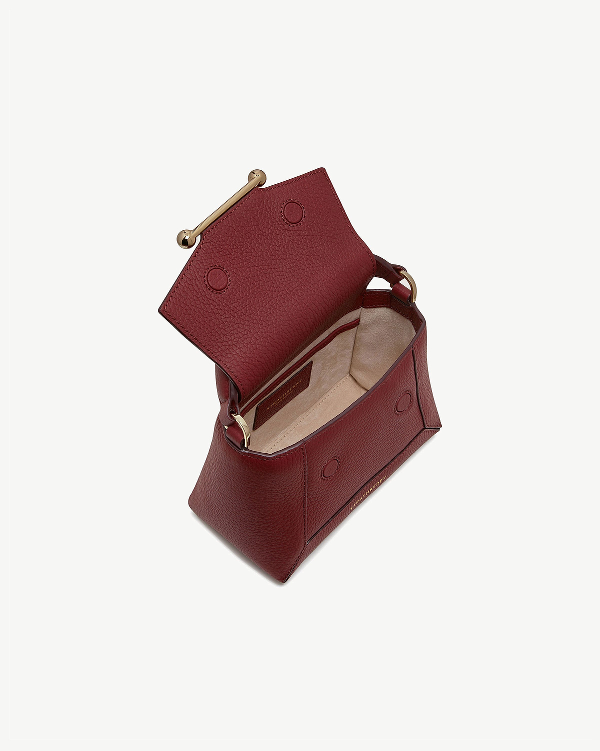 Oxblood leather nano bag open, showing beige suede interior and gold bar