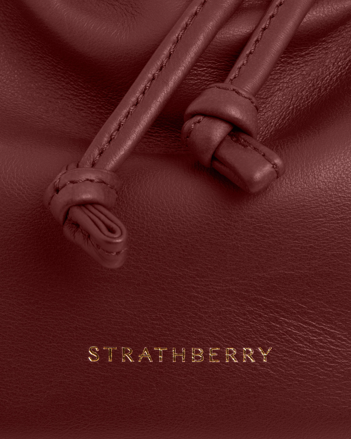 Oxblood leather with stitched knotted drawstrings, textured grain and gold Strathberry logo