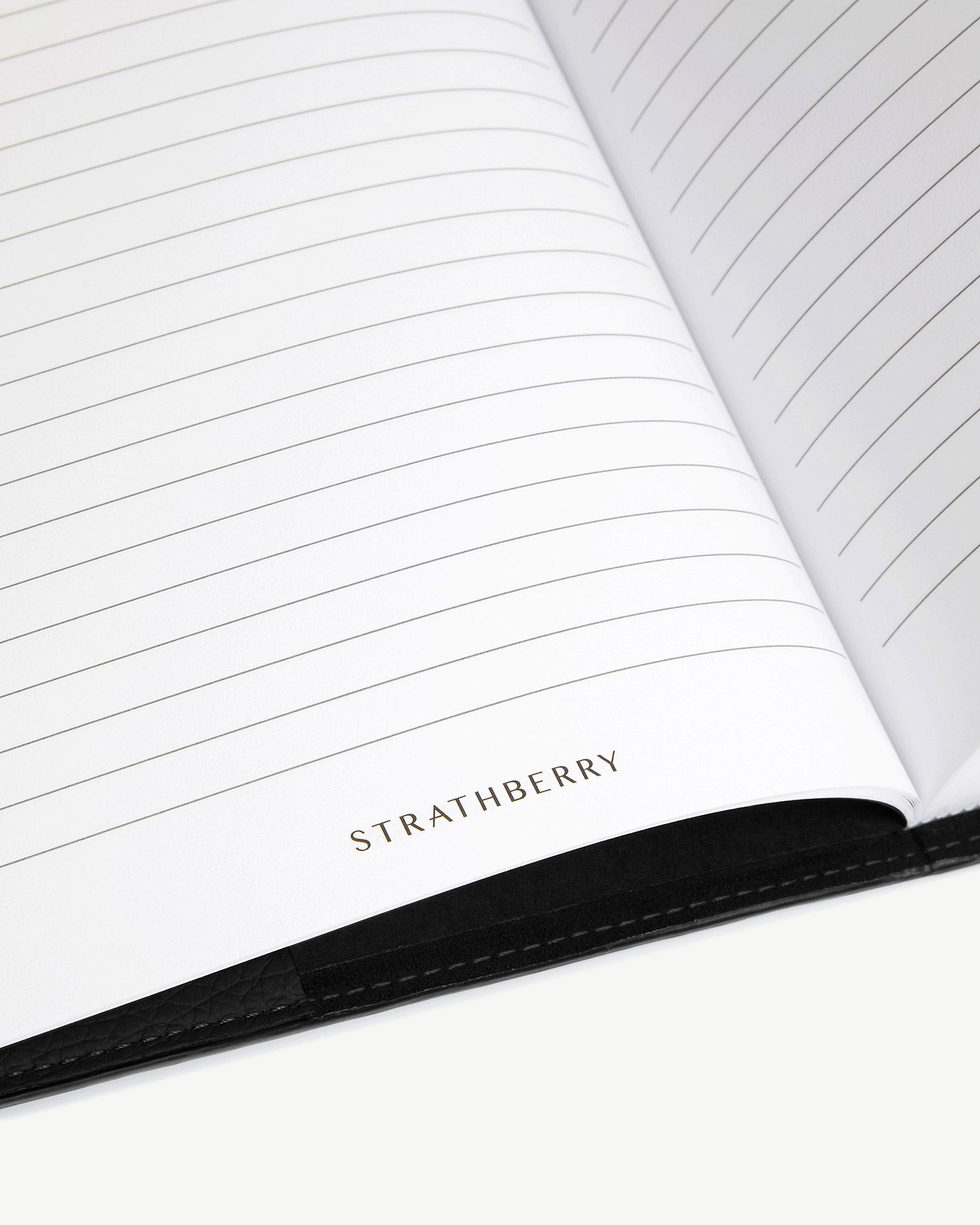 Open lined notebook with Strathberry logo and visible black leather cover edge.