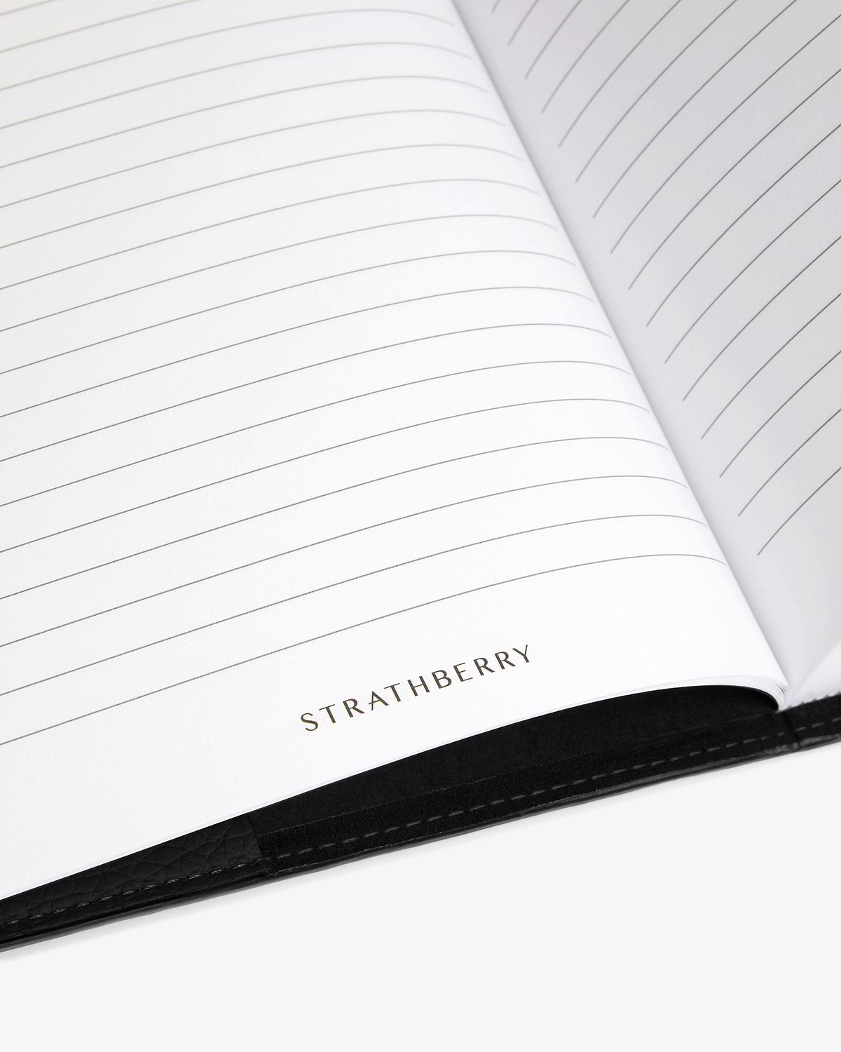 Open lined notebook with Strathberry logo and visible black leather cover edge.