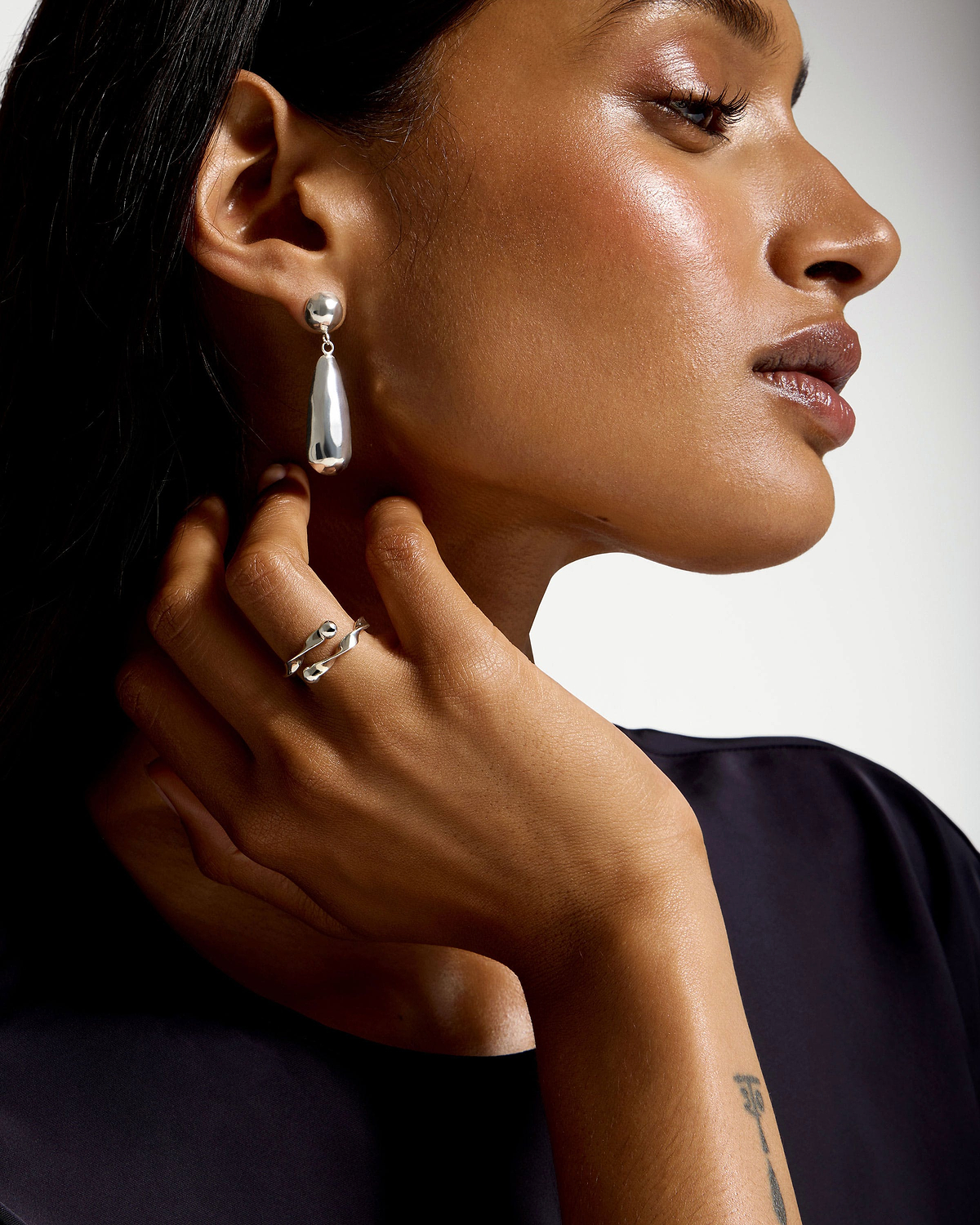 Model side profile wearing sterling silver Jasmine drop earrings and a silver ring.