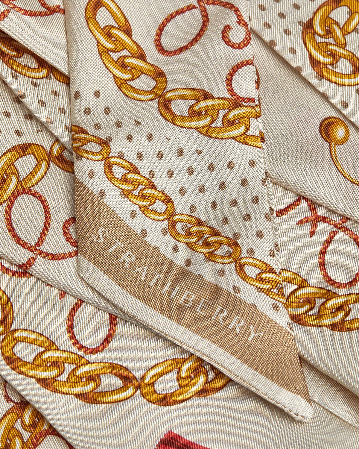 Caramel long silk skinny scarf with diamond chain print and visible Strathberry logo.