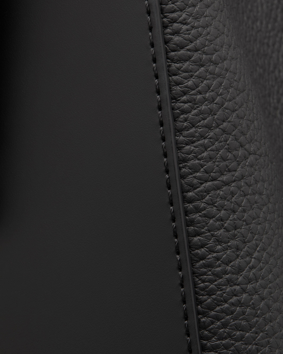 Close-up of black pebbled and smooth leather panels with stitched seam.