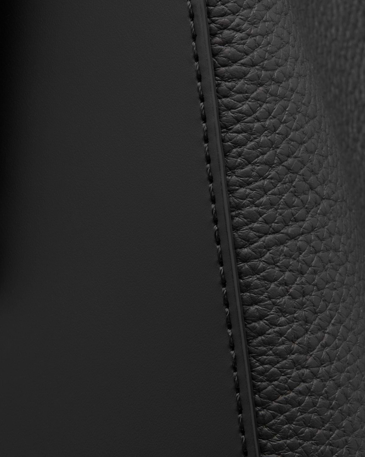 Close-up of black pebbled and smooth leather panels with stitched seam.