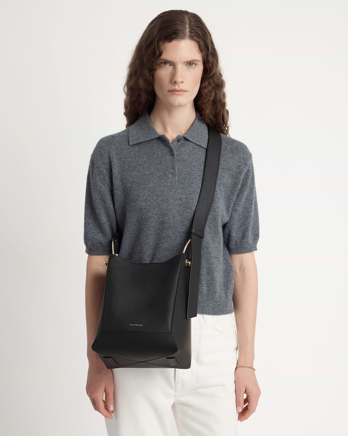 Model wearing black midi bucket bag with wide shoulder strap and gold hardware.