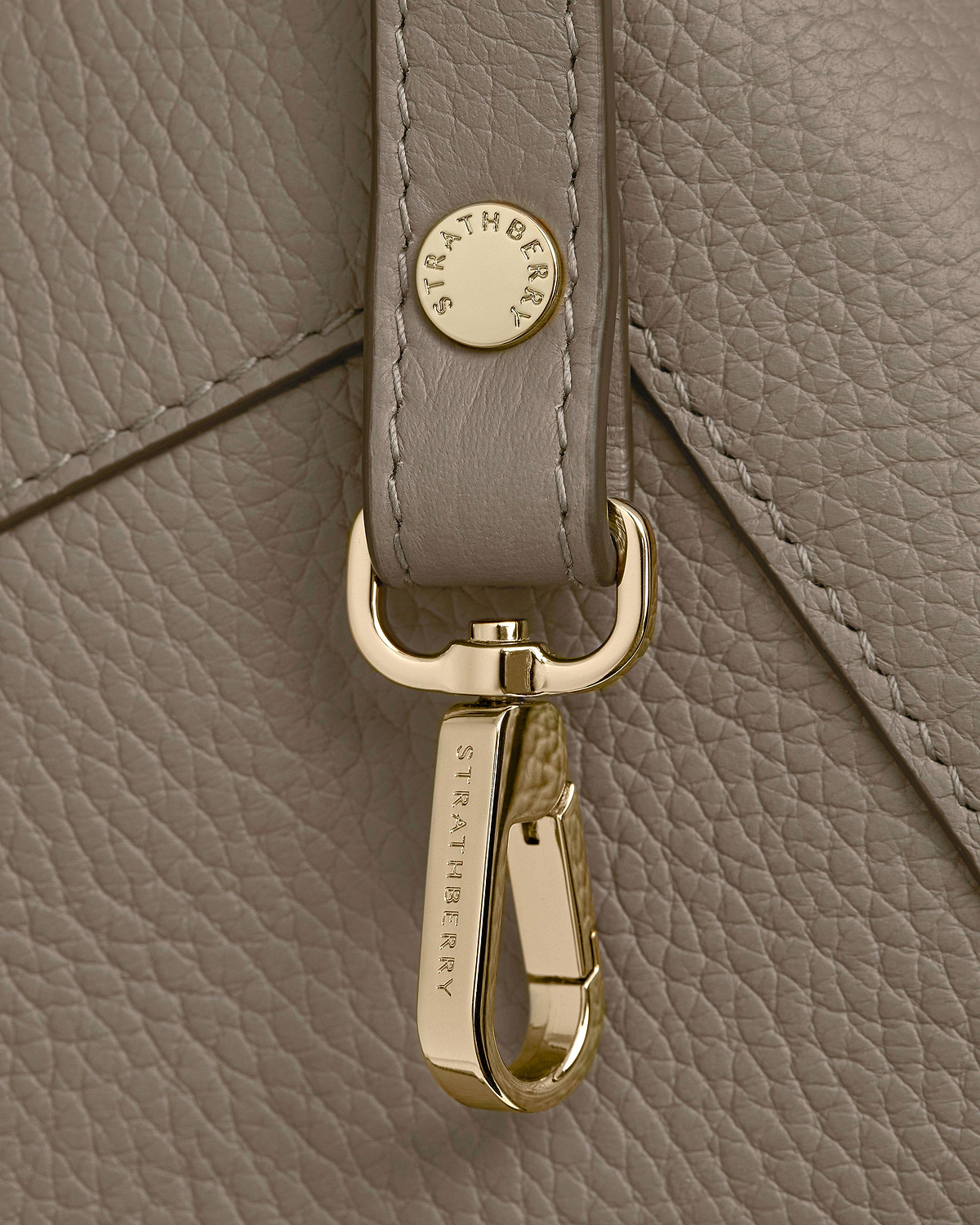 Taupe pebbled leather with gold Strathberry clasp and strap hardware detail.