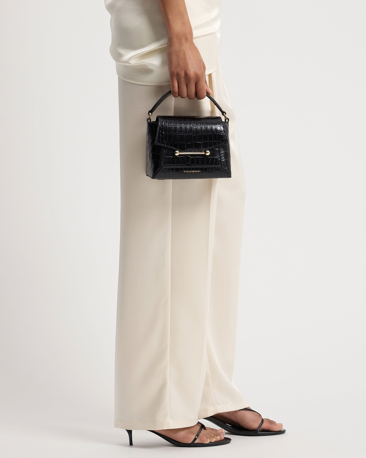 Hand holding Strathberry Mosaic Nano bag in soft croc with gold hardware.