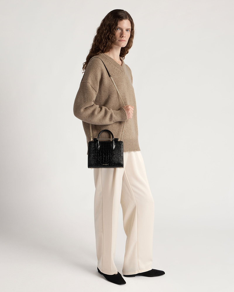 Model wearing beige jumper holding black croc mini tote with gold chain strap