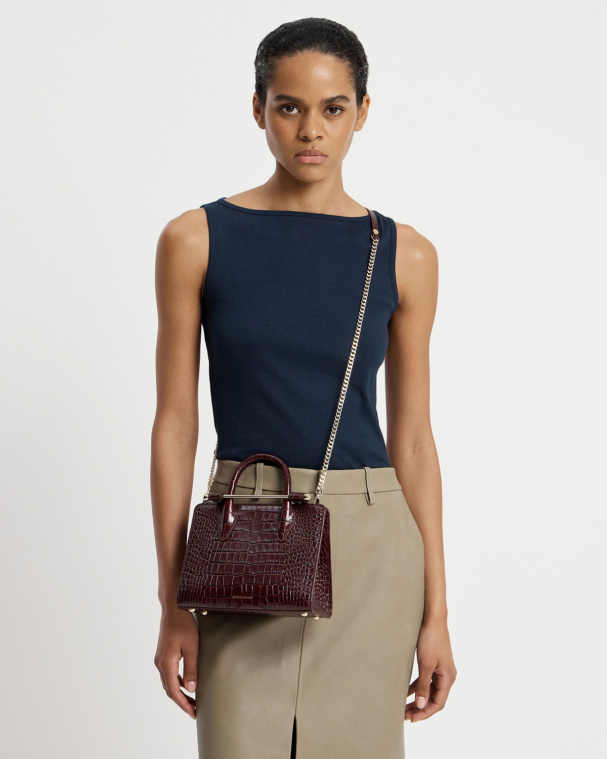 Model wearing a mini croc tote crossbody with gold chain strap and top handles.