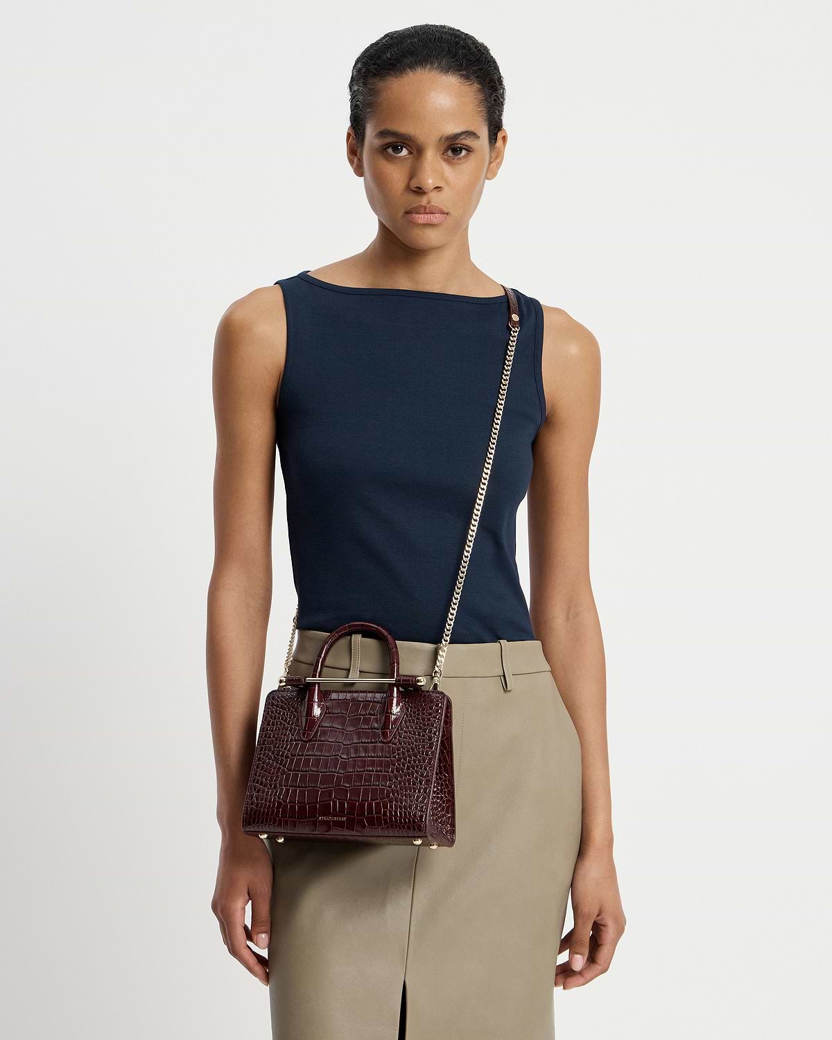 Model wearing a mini croc tote crossbody with gold chain strap and top handles.
