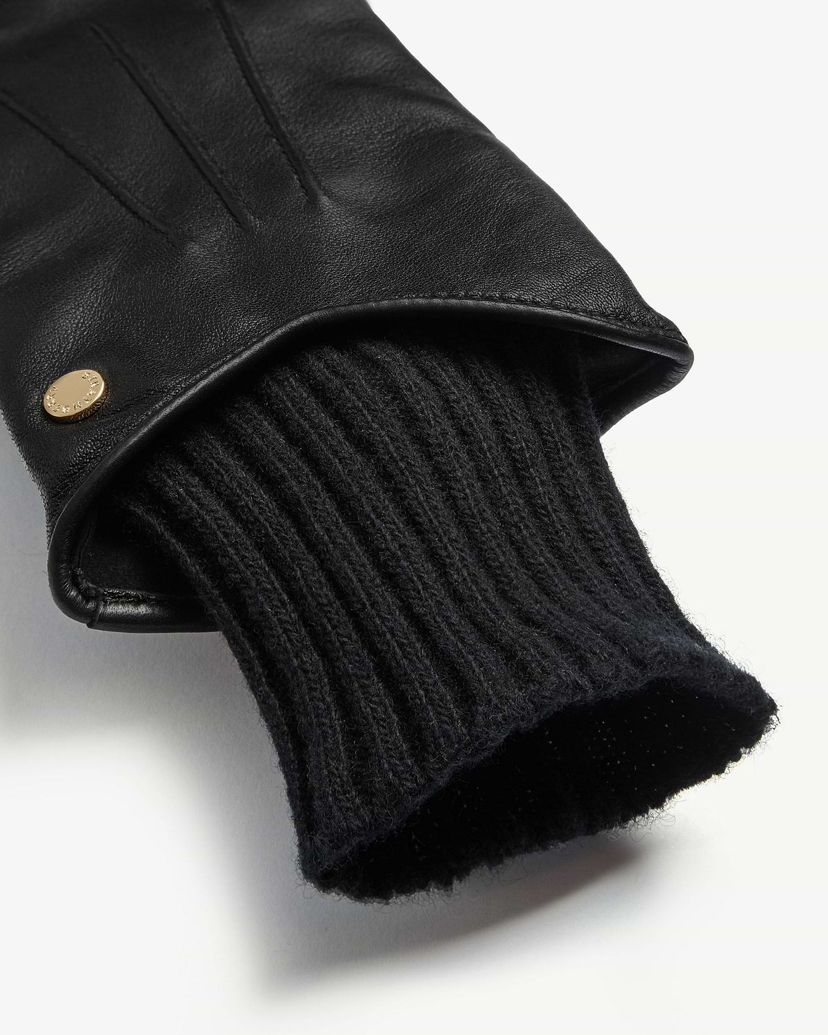 Close-up of black leather glove showing ribbed knit cuff and gold stud.