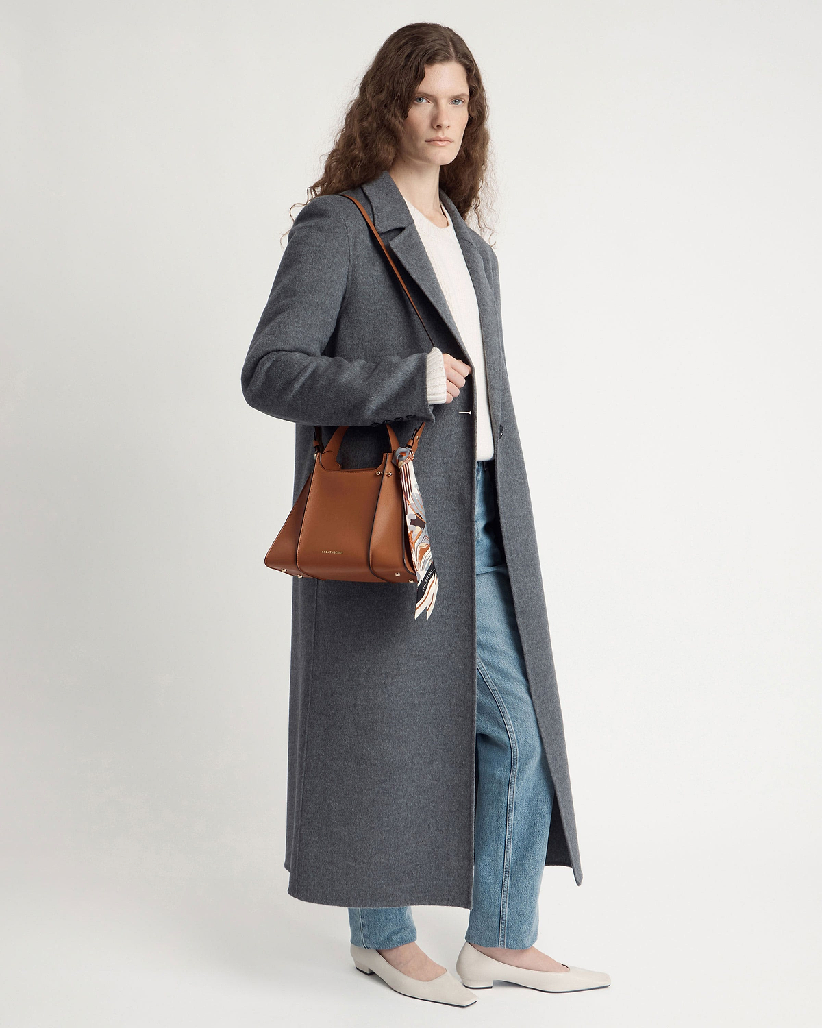 Model wearing tan Arkshell shoulder bag with patterned silk scarf and long grey coat.