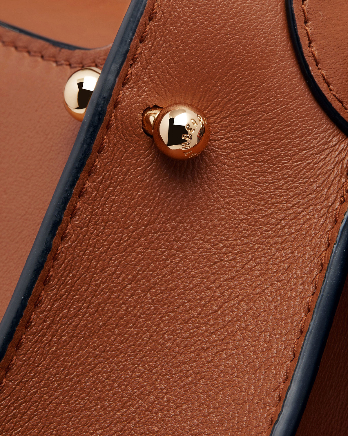 Tan Arkshell leather close-up showing gold stud, dark edge trim and stitching
