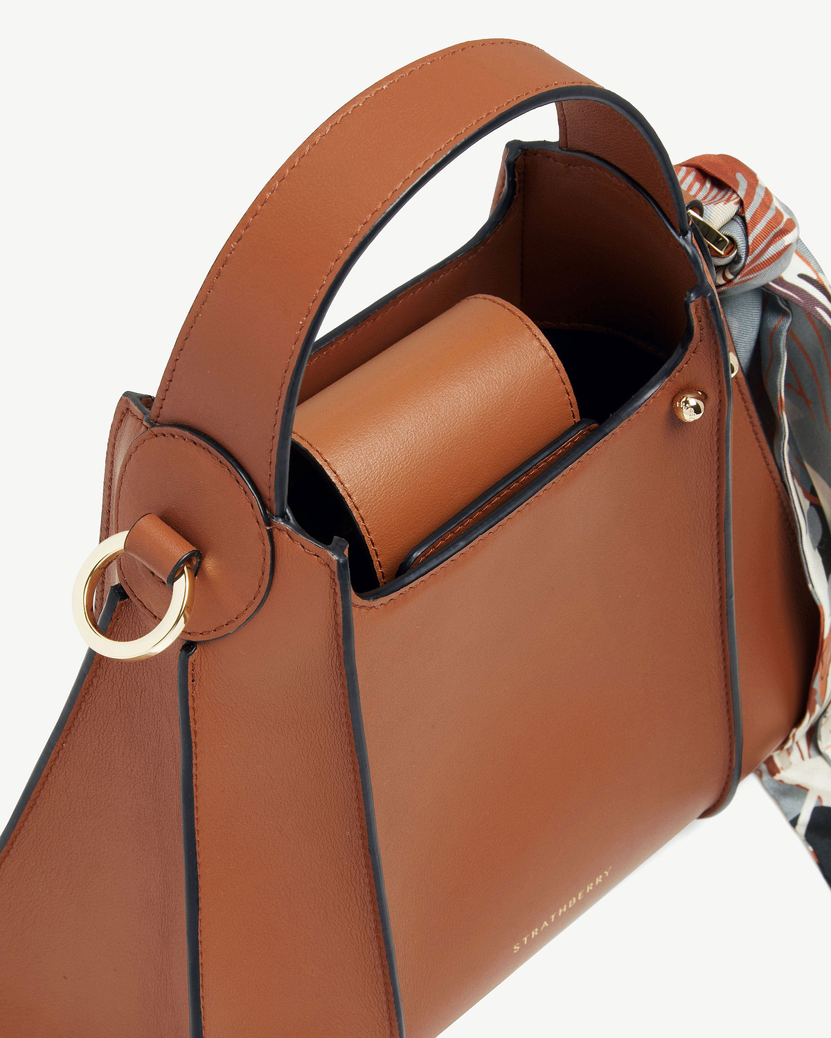 Tan Arkshell bag by Strathberry with top handle and patterned scarf.